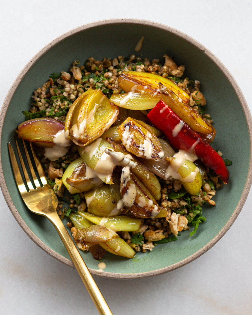 Turmeric shallots with crispy buckwheat and beans drizzled with tahini in a bowl with fork