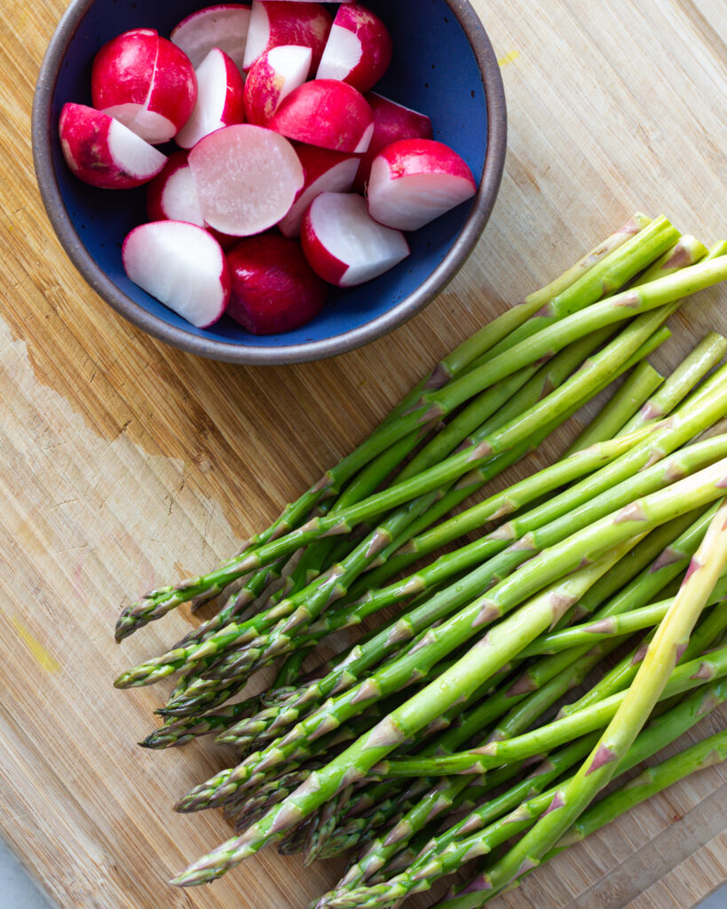 trimmed and sliced radishes in a bowl and prepped asparagus on a cutting board