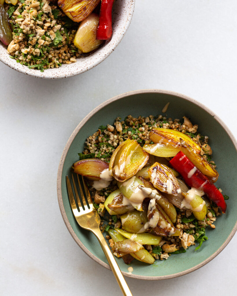 Turmeric shallots with crispy buckwheat and beans drizzled with tahini in bowl with fork