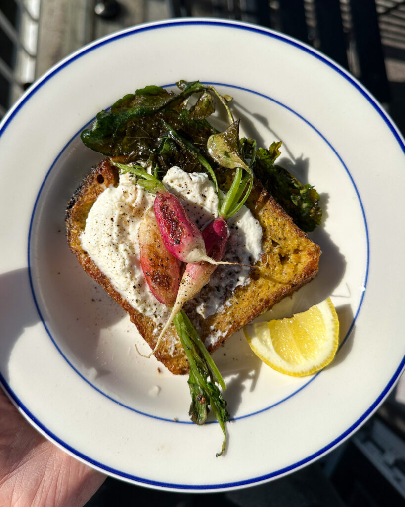 Savory french toast topped with ricotta and breakfast radishes plated with a wedge of lemon on the side