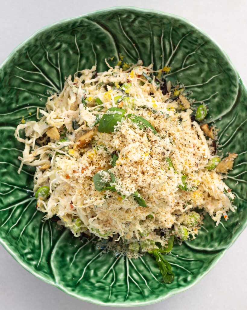 Overhead view of finished salad with charred lemon dressing topped with grated walnuts and herbs, served in a cabbage bowl