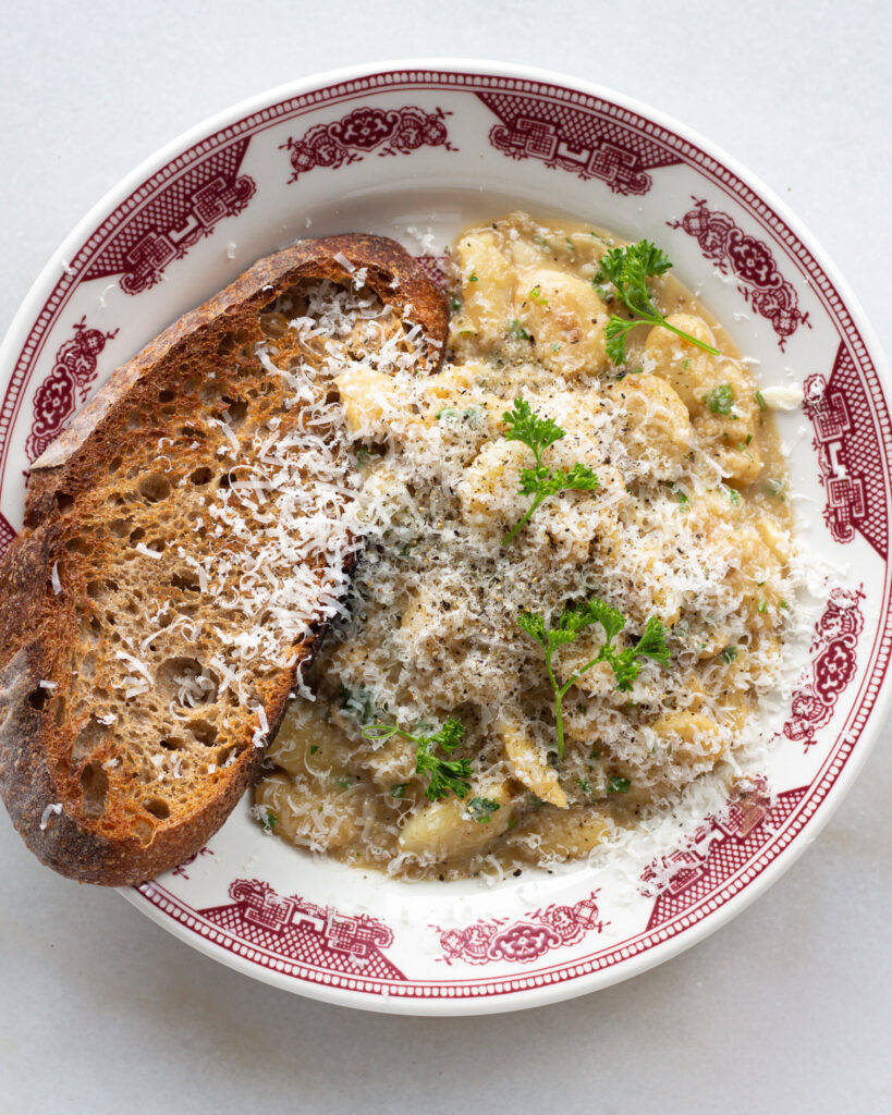 Garlic beans with toast server on a plate, topped with shaved parmesan cheese and parsley