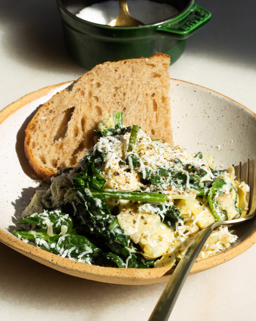 Spinach Artichoke Bowl served for one, with slice of bread and a fork. A salt cellar with a gold spoon is in the background.