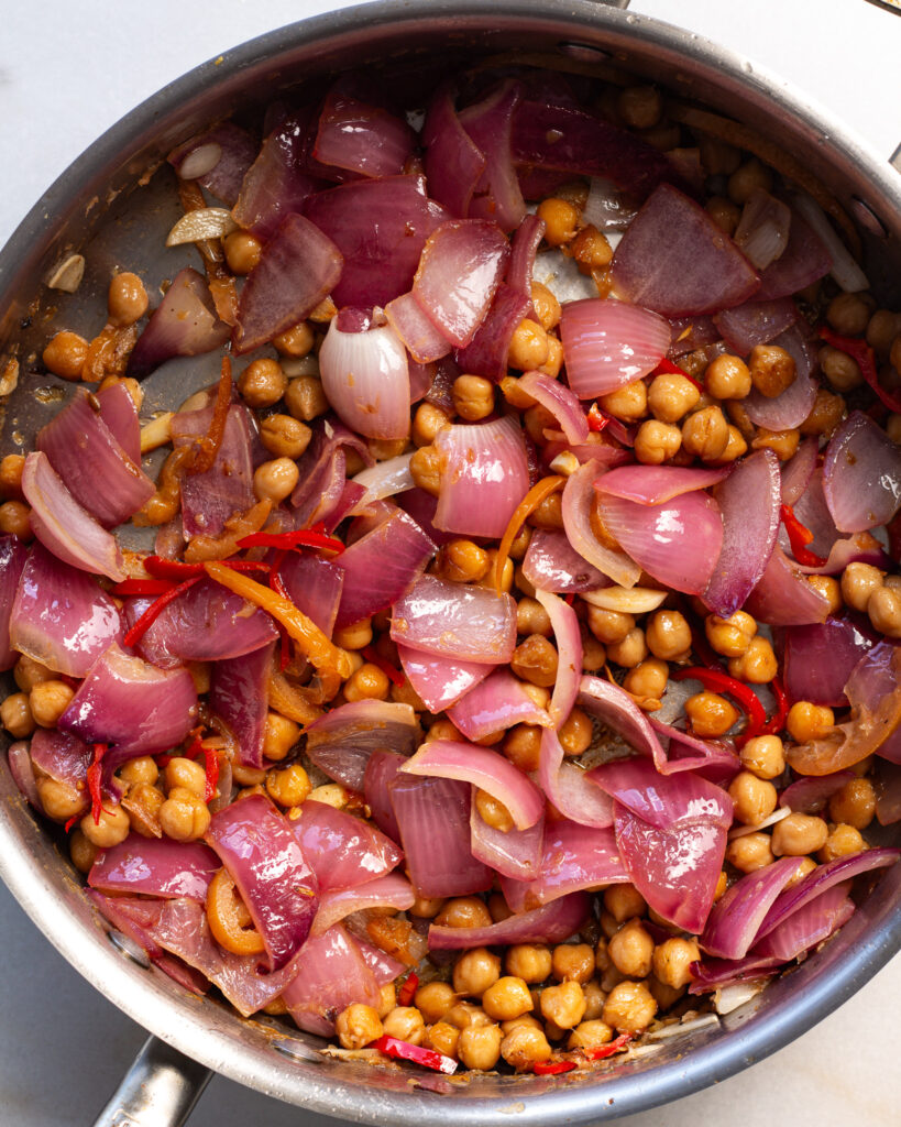 red onion, chickpeas, garlic, fresno peppers and preserved lemon being caramelized in a pan 