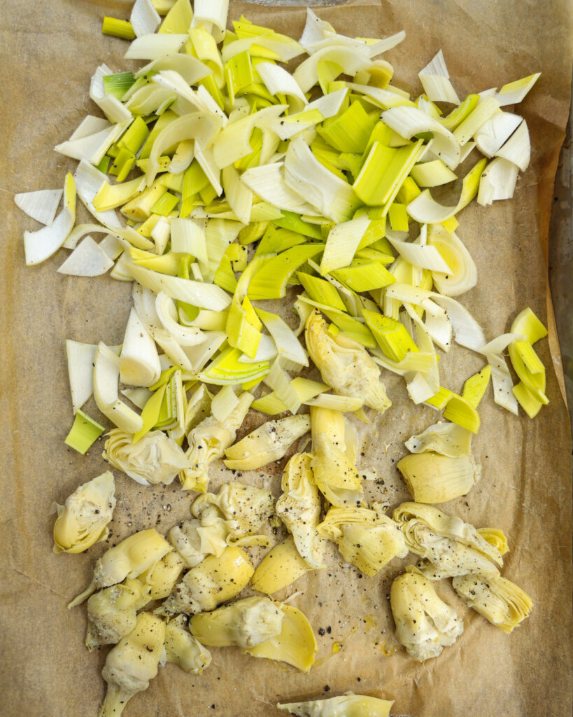 Artichokes and leeks on a baking sheet.