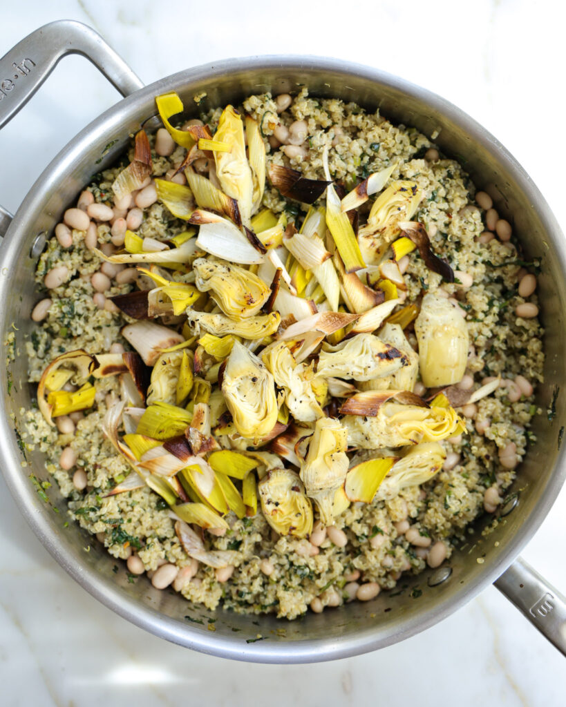 Roasted artichokes and leeks added to a pot of quinoa.