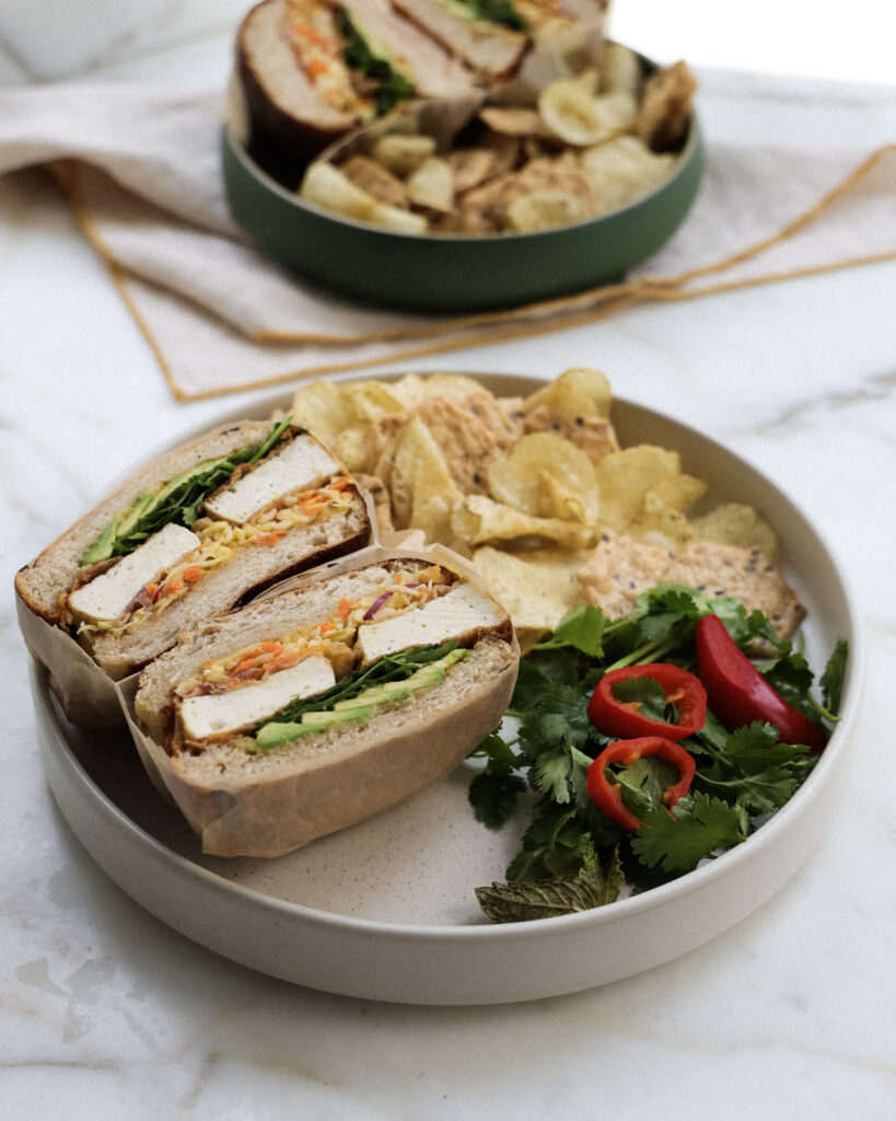 baked tofu sandwich served with chips and veggies.