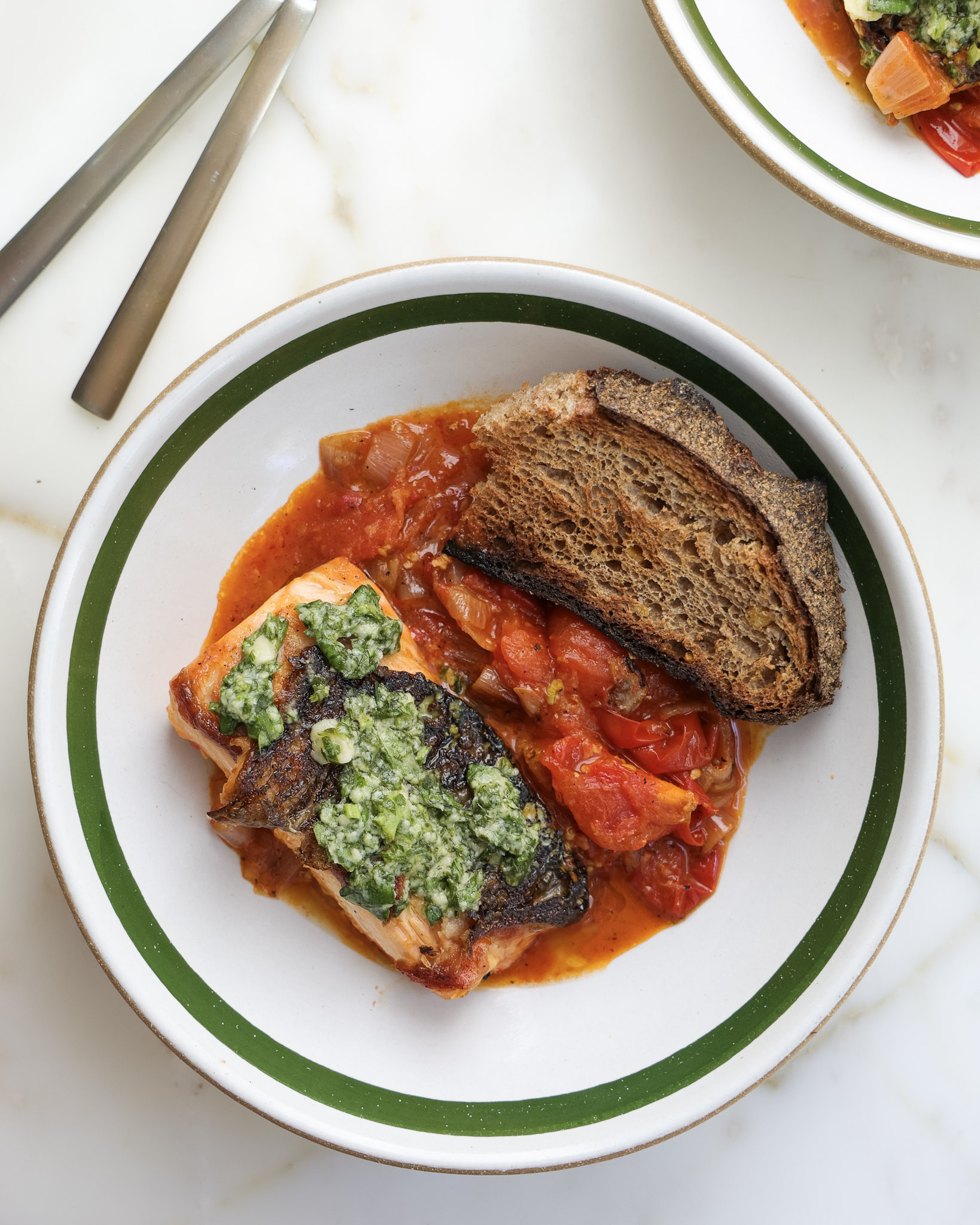 Basil tomato salmon in a bowl with a slice of sourdough.