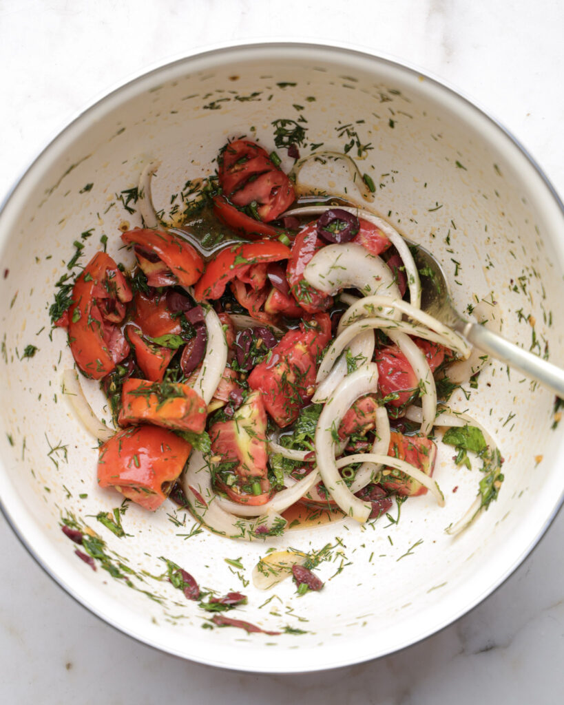 Tomatoes, onion, and herbs added to a bowl.