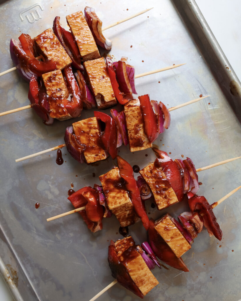 Glazed tofu skewers uncooked on a baking sheet.