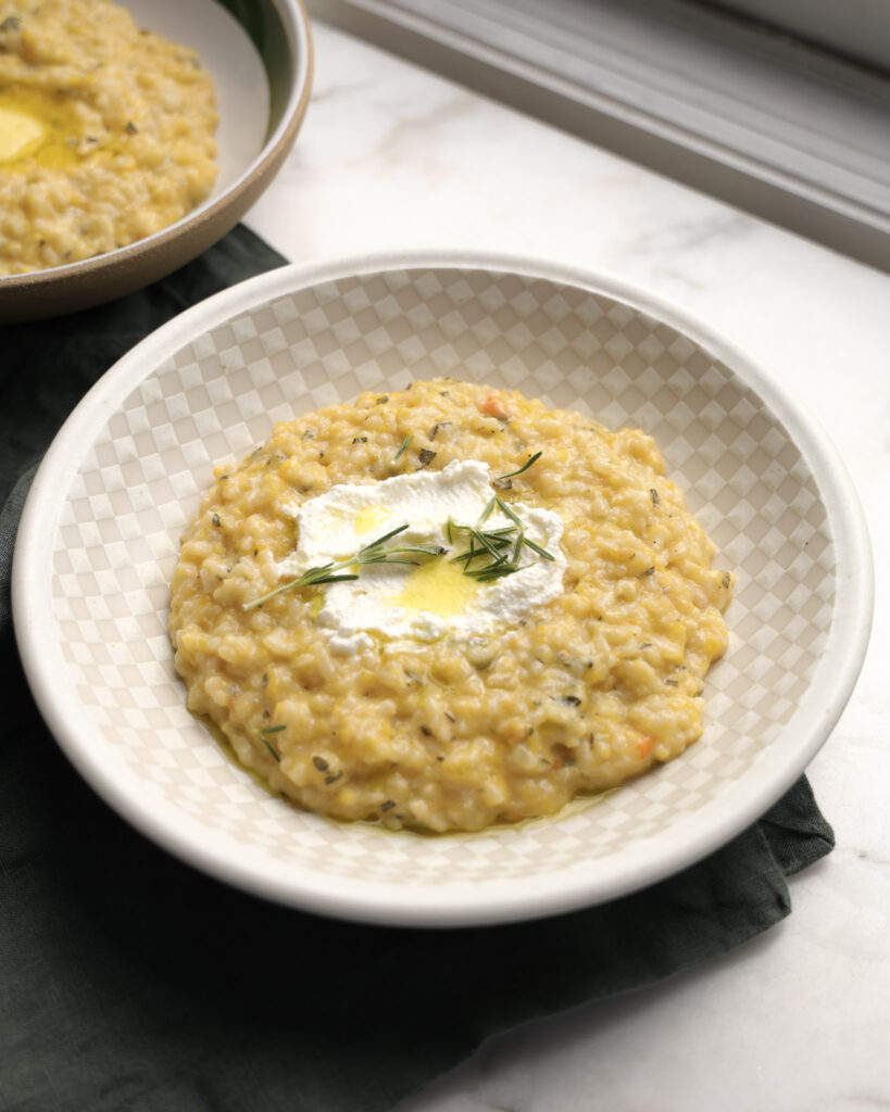 Squash-zotto in a bowl topped with herbs and ricotta.
